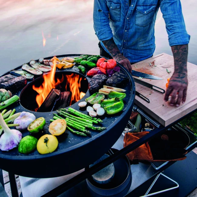 <think> Got it, let's write the alt text. First, identify what's visible. The image shows a person grilling with various veg…